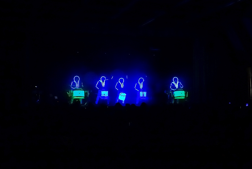 5 Schlagzeuger auf Bühne, beleuchtet in blauem LED Licht, Hintergrund schwarz